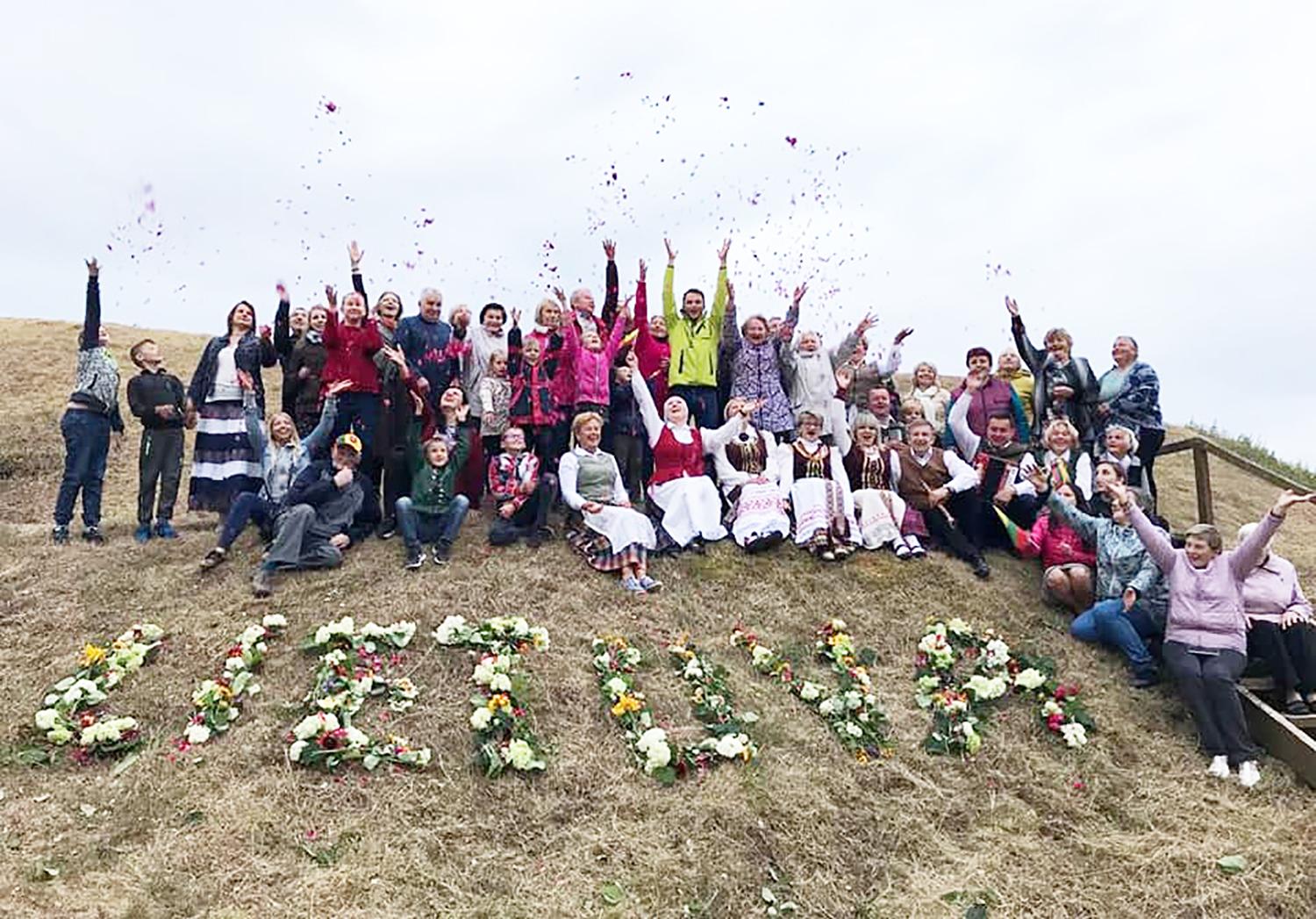 Visi mes esam Lietuva / Piliakalnio papėdėje iš gėlių ir žolynų visi dėliojo žodį „Lietuva“ ir įsiamžino bendroje nuotraukoje.